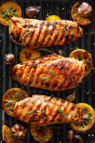 Grilled chicken breasts with thyme, garlic and lemon slices on a grill pan, top view