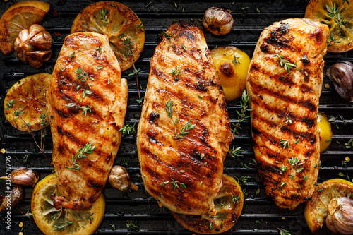 Grilled chicken breasts with thyme, garlic and lemon slices on a grill pan, top view