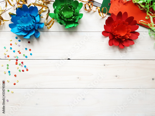 The child made crafts with his own hands. Colorful handmade flowers from multi-colored paper. Flowers, cardboard, ribbon. Art creativity on a white wooden table. Diy crafts, top view, copy space