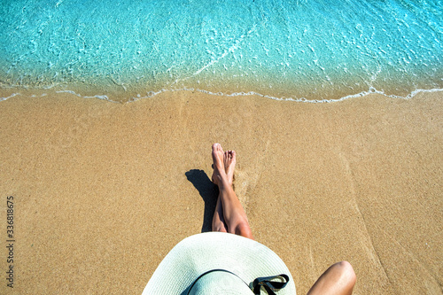 Long slim young woman legs relaxing lying down and sunbathing on sand tropical beach under hot sun in summer. Skincare, sun aging protection and sea travel concept.