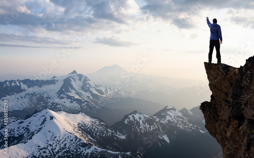 Adventure, Explore and Lifestyle Concept Composite. Adventurous Man Hiker With Hands Up on top of a Steep Rocky Cliff. Sunset or Sunrise. Landscape Taken from Washington, USA.