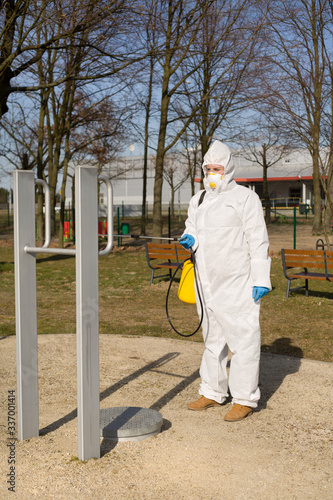 Kobieta w kombinezonie ochronnym dezynfekuje sprzęt sportowy w parku