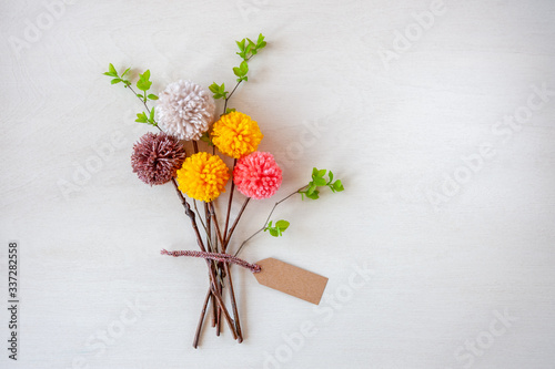 Abstract bouquets of flowers made of colorful pom poms. Easter bunny made of yarn on wooden background. Spring concept. Copy space for text. Top view. Soft focus.