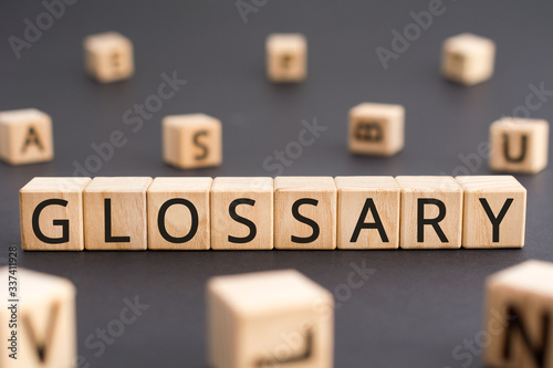 Glossary - word from wooden blocks with letters, alphabetical list of terms glossary concept, random letters around black background