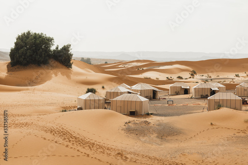 Contemporary luxury glamping camp in Morocco Sahara desert. Sand dunes around. Many white modern eco tents.