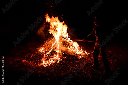 A man throws dry leaves into a large fire, night.