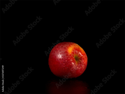 Juicy red apple covered with water droplets, photo on the black background in the light of the lamp