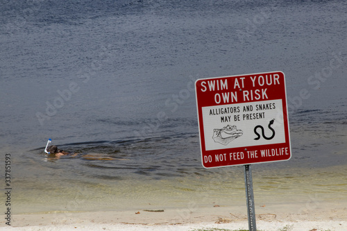 Warning sign at a Florida lake: Swim At Your Own Risk, Alligators and Snakes May Be Present