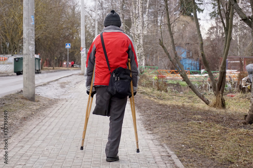  A man on one leg, with two crutches, is walking along the sidewalk.