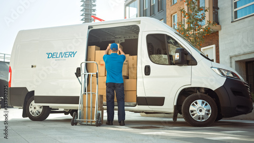 Delivery Man Uses Hand Truck Trolley Full of Cardboard Boxes and Packages, Loads Parcels into Truck / Van. Professional Courier / Loader helping you Move, Delivering Your Purchased Items Efficiently