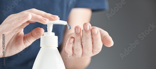 Female hands using hand sanitizer gel pump dispenser on a gray background.