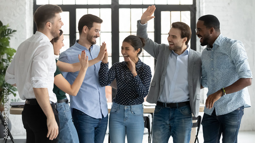 Overjoyed multiracial colleagues have fun celebrate shared business victory or win at workplace, happy diverse multiethnic businesspeople engaged in funny teambuilding activity in office together