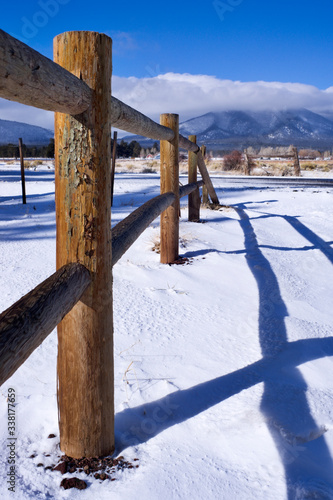 A wooden Post Fence and Snow with snow covered ground and a blue sky with some clouds
