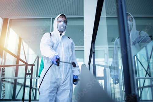 Shot of male person in white chemical protection suit doing disinfection of public areas to stop spreading highly contagious corona virus. Stop coronavirus or COVID-19.