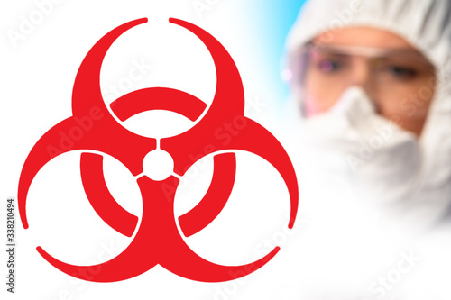 A large red biohazard sign and the face of a chemist in a protective mask. Medical quarantine. Security measures during quarantine. Preventing the spread of the disease. Epidemic.