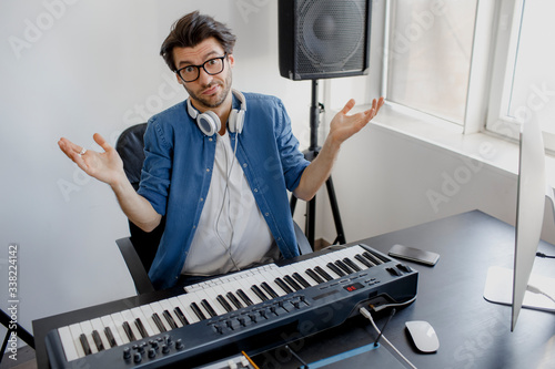 He looks into the camera and shrugs his hands. He is bewildered and does not know what to do. Bad employee. Male music arranger composing song on audio equipment in digital recording studio.