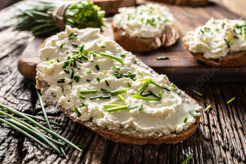 Close-up of bread slice with traditional Slovak bryndza spread made of sheep cheese with freshly cut chives placed on rustic wood