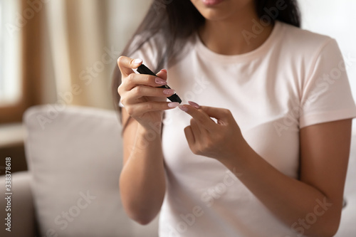 Close up image, young woman sitting on couch at home holding portable glucose meter electronic device checkup test blood sugar. Patient with diabetes mellitus health problem, modern tool usage concept
