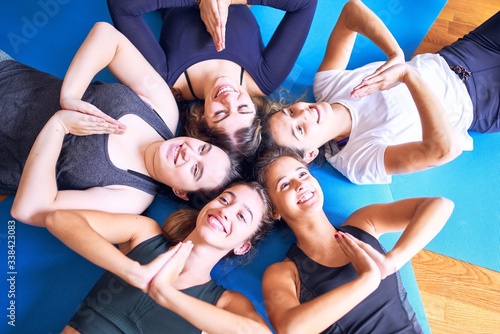 Young beautiful group of sportswomen practicing yoga lying down doing circle on the floor. Smiling happy doing prayer at gym