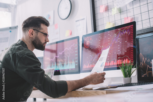 Side view of information security analyst looking at charts near graphs on computer monitors in office