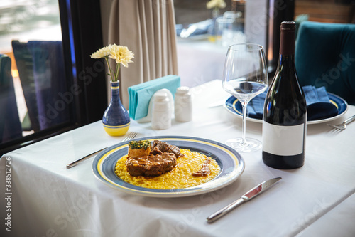 Italian cuisine dish Ossobuco Alla Milanese with veal stew and risotto on the white table with a bottle of wine, side view