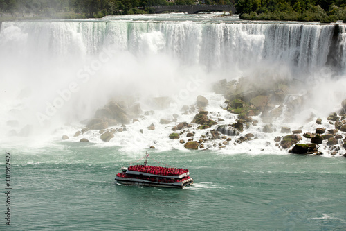 Niagara Falls tour boat red rain suits waterfall. Waterfalls at border of US state of New York and Canadian province of Ontario. Drains Lake Erie into Lake Ontario. 