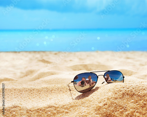 Empty sand beach in front of summer sea with sunglasses, happy family and copy space