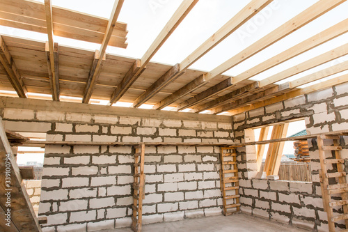 Building site of a house under construction. Unfinished house walls made from white aerated autoclaved concrete blocks. Scaffolding for workers assembled from boards and Euro-pallets.