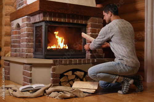 Man putting dry firewood into fireplace at home. Winter vacation