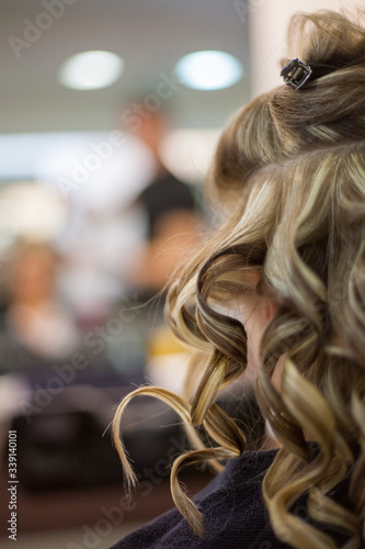 Hairdresser curling a blond woman's hair in professional hairdressing salon or barbershop , seen from behind the customer, unrecognizable.