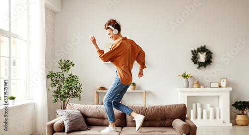 Cheerful woman listening to music and dancing on soft couch at home in day off.