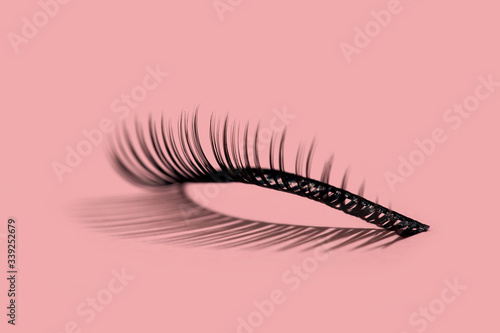 A pattern of separate false lashes on pink background with hard light makes shadow