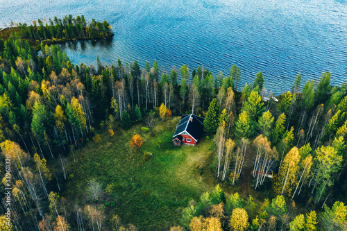 Aerial top view of red log cabin or cottage with sauna in spring forest by the lake in Finland