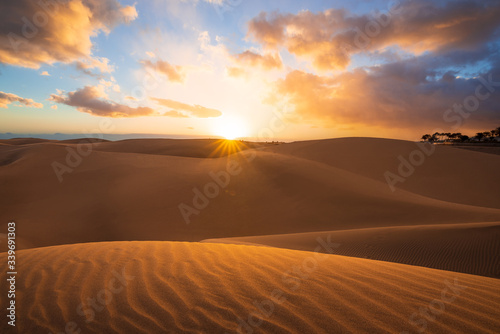 Sunset in the desert, sun and sun rays, Beautiful clouds on blue sky. Golden sand dunes in desert in Maspalomas, Gran Canaria, Canary islands, Spain 