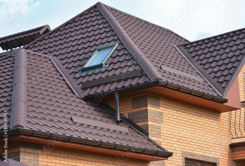 Complex roof design, metal tiled expensive roofing construction with a skylight, snow guards, chimney of a brick house.