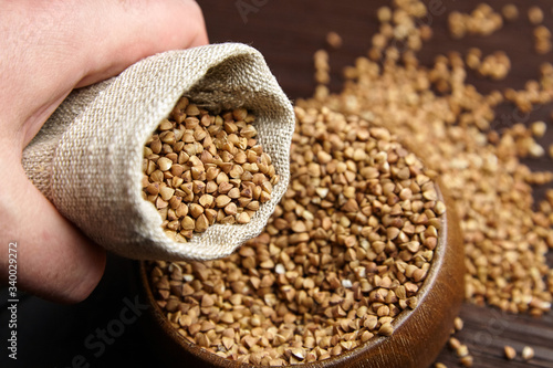 Buckwheat groats (hulled seeds) in bowl and burlap bag on wooden table