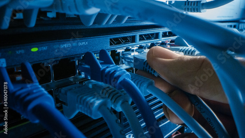 Macro Shot: IT Administrator Plugs in RJ45 Internet Connector into LAN Router Switch. Information Communication Network in Data Center with Cables Connected to Modem Ports with Blinking Lights