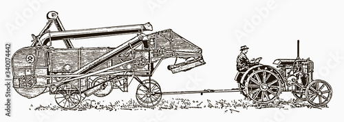 Historical farmer sitting on antique tractor pulling an attached thresher, in side view. Illustration after an engraving from the early 20th century