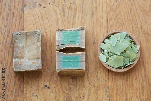 Flat lay overhead shot of an Aleppo bar soap and cuts showing its green color on a wooden background.