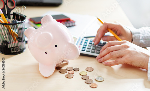 Women counting coins on calculator taking from the piggy bank. Use last savings, unemployment and bankruptcy concept.