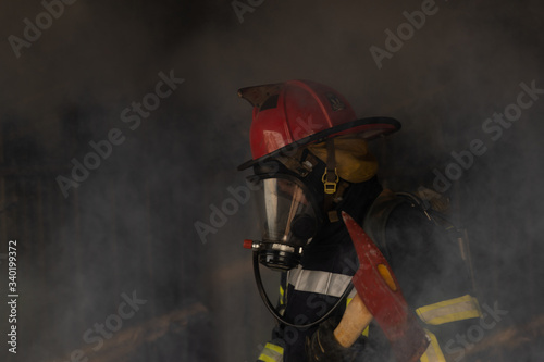 Asian fireman holding Axe confident with smoke, fire burning hard in background. Fireman career concept.