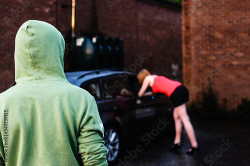 Man watches a prostitute talking to a potential customer in a car (posed by models)