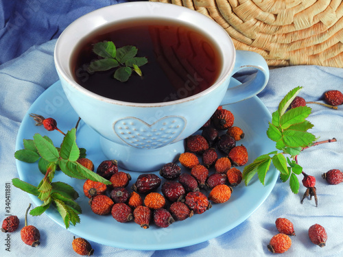 Tea with rose hip fruit in wide blue cup decorated with young rose twigs. Natural vitamin, antioxidant and diuretic drink. 