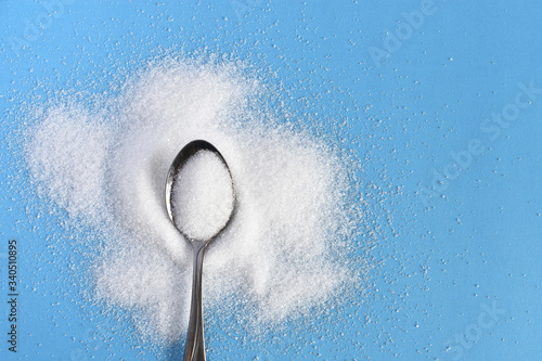 A top view image of a metal spoon and white sugar on a bright blue background. 