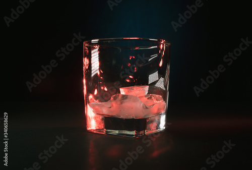 Szklanka z lodem na czarnym tle w czerwonych refleksach.