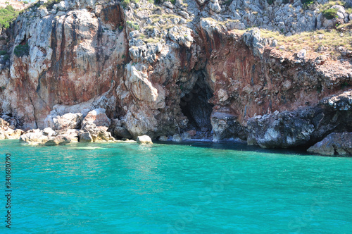 Clear turquoise sea and rocks on the shore. In the rock, the entrance to the cave.