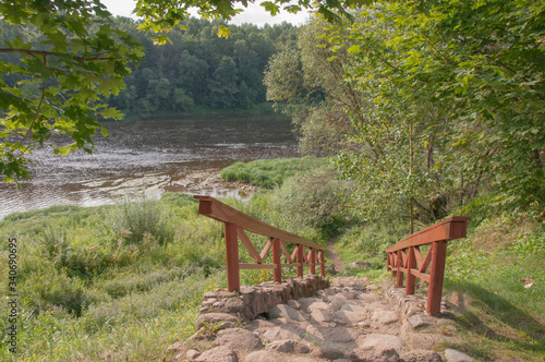 A stone staircase with wooden railings in the deciduous forest leading to a large river.
