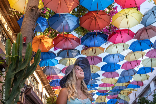 blond young woman in dark blue hat and street of colorful umbrellas above her in north part of Nicosia the capital city of Cyprus