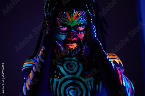 african man with fluorescent body art suffer from headache, hold head, stand with closed eyes. UV body art