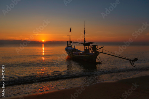 A folk fishing boat is parked on the coast in the morning while the sun is rising.